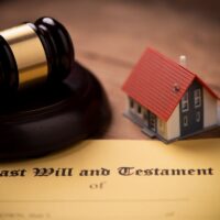 A gavel beside a model house on a 'Last Will and Testament' document.